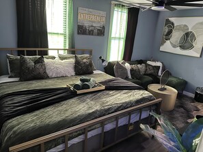 A bedroom with a bed, pillows, a bedside table, a lamp, and a wall with a poster.