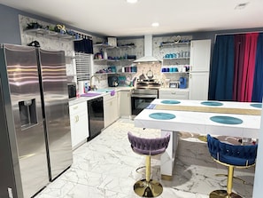 A modern kitchen with a built-in refrigerator, a stove, and a sink. There is a dining table with two bar stools.