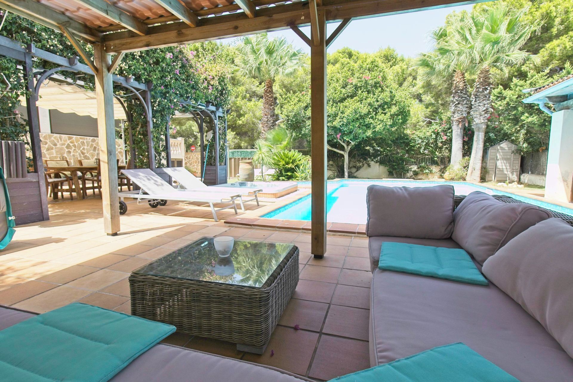 A covered outdoor area with a pool, lounge chairs, and a sofa with cushions.