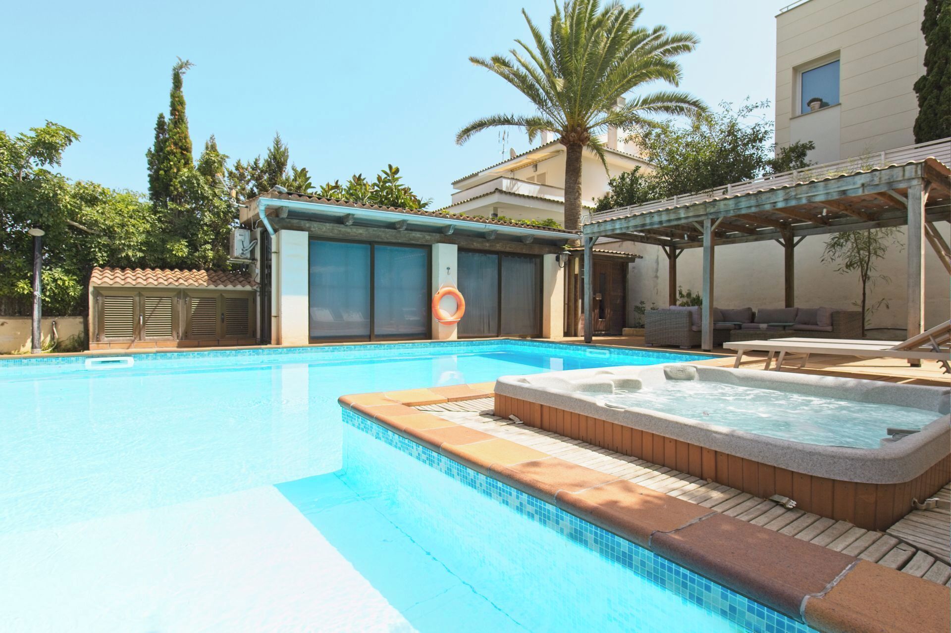 A swimming pool with a hot tub, outdoor seating, and a covered area.