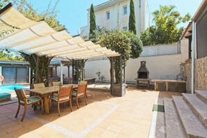 Une terrasse avec une table et des chaises, un barbecue et une piscine.