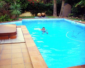 En swimmingpool med fliseterrasse og et lille skur i baggrunden.