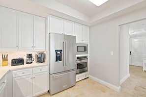 A modern kitchen with white cabinets, a stainless steel refrigerator, a microwave, and a coffee maker. - Indigo East 402 (Pensacola)