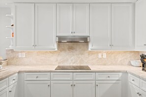 A kitchen with white cabinets, a stainless steel range hood, and a marble countertop. - Indigo East 402 (Pensacola)