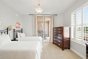 Un dormitorio con dos camas, un aparador, una lámpara y vistas a través de un ventanal.