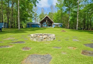 Una cabaña con un hogar de piedra, rodeada de un césped cuidado y árboles.