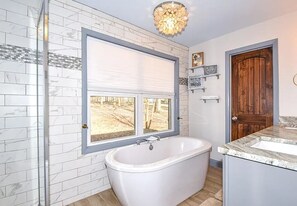 Un baño con una bañera independiente, un ventanal con vistas al exterior y una puerta de madera.