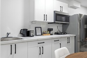 Een moderne keuken met witte kasten, een roestvrijstalen koelkast, een magnetron en een koffiezetapparaat.