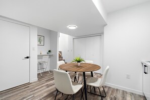 Een moderne, minimalistische kamer met een ronde houten tafel, witte stoelen en een potplant.