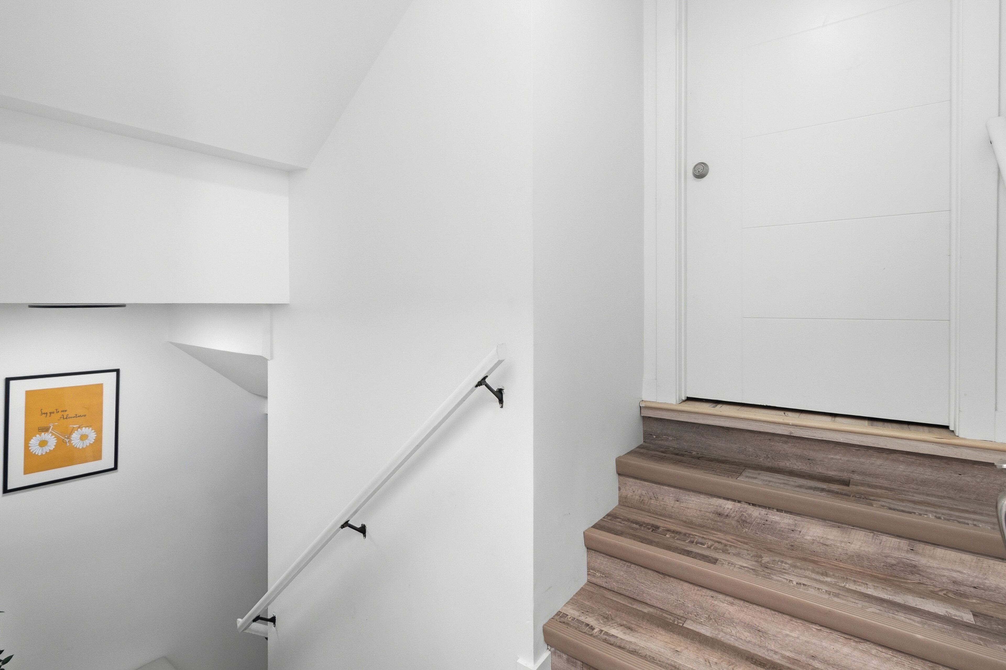 A staircase with wooden steps and a white handrail, leading to a white door.