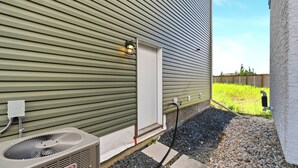 Una unitat de climatització exterior, una porta metàl·lica i una mànega connectada a una font d'aigua.