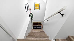 Una escala amb acabat de fusta, un estri amb lletra blanca i un quadre encimbellat a la paret.