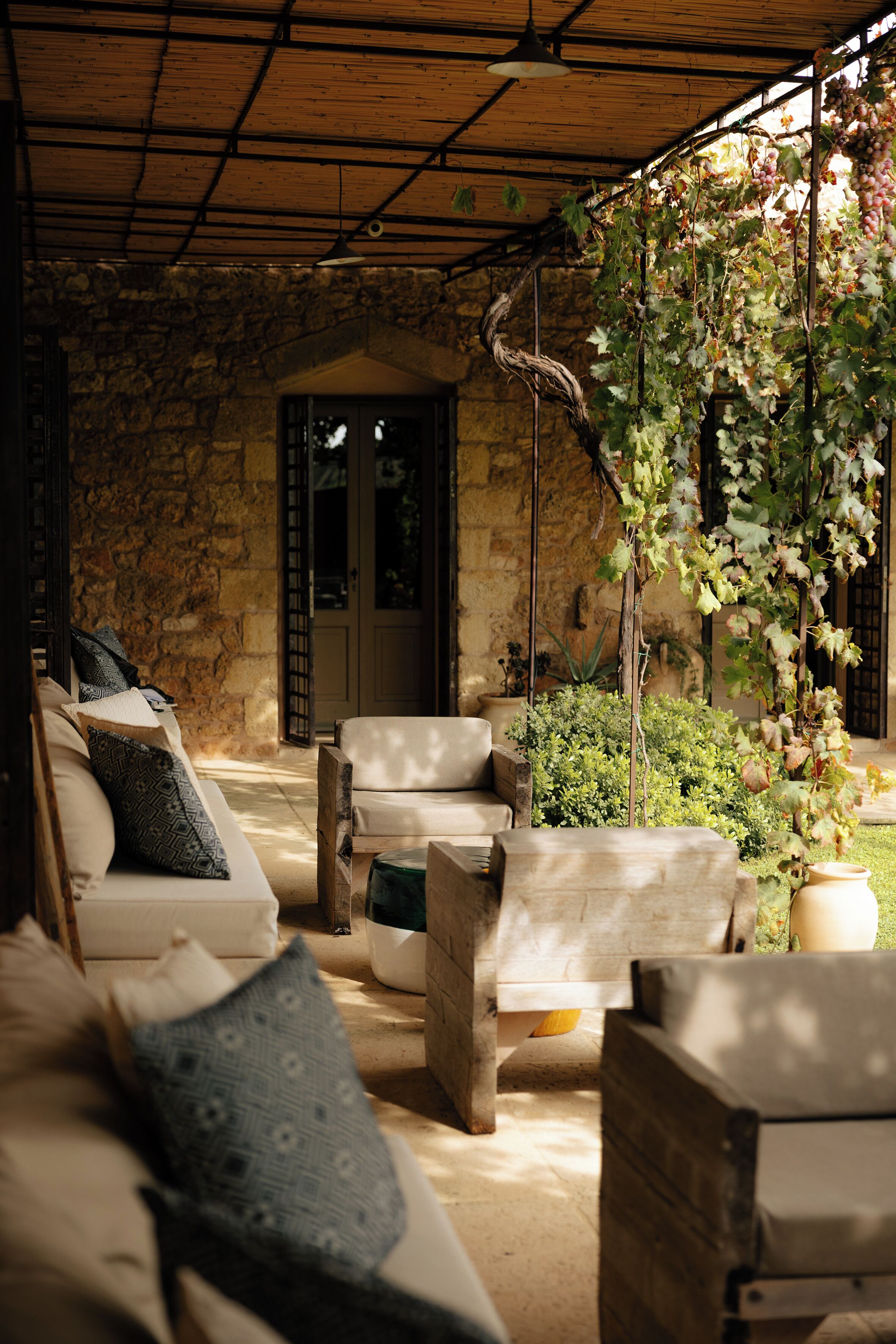 Un área de estar al aire libre cubierta con paredes de piedra y techo de madera, que incluye un sofá y sillones con cojines estampados.