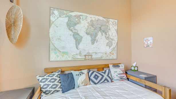 A bed with patterned pillows, a world map on the wall, and a small desk with a tissue box. - Walk to the Alamodome! Quirky Gem w/ Private Patio (San Antonio)