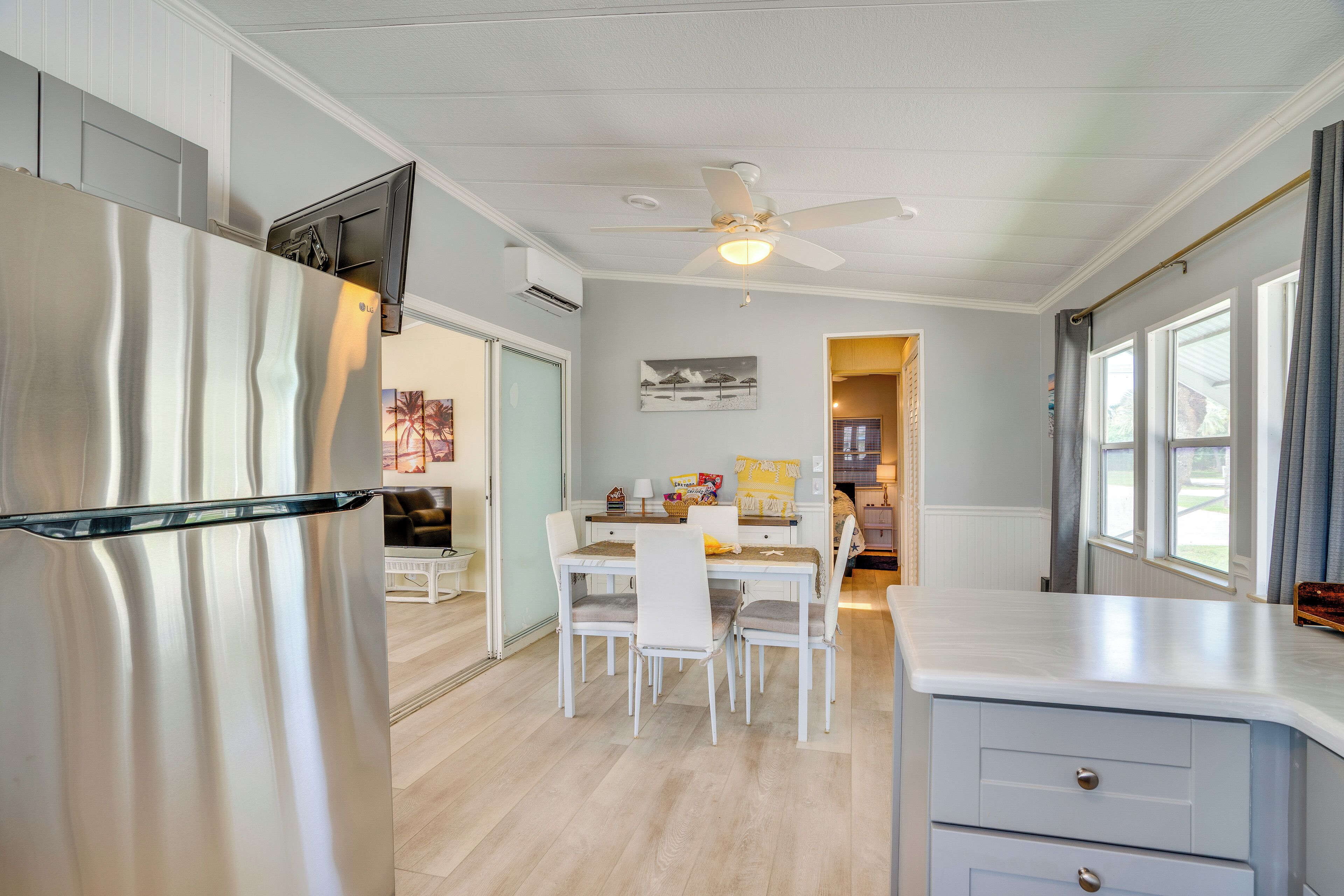 A modern kitchen with a stainless steel refrigerator, white cabinetry, and a dining area with a table and chairs.