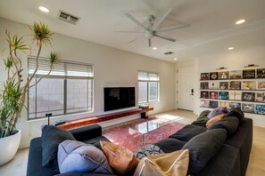 A modern living room with a flat-screen TV, a ceiling fan, and a wall of framed pictures. - Relax Poolside! Retreat 2 Mi to Santan Mtn Casino (Chandler)