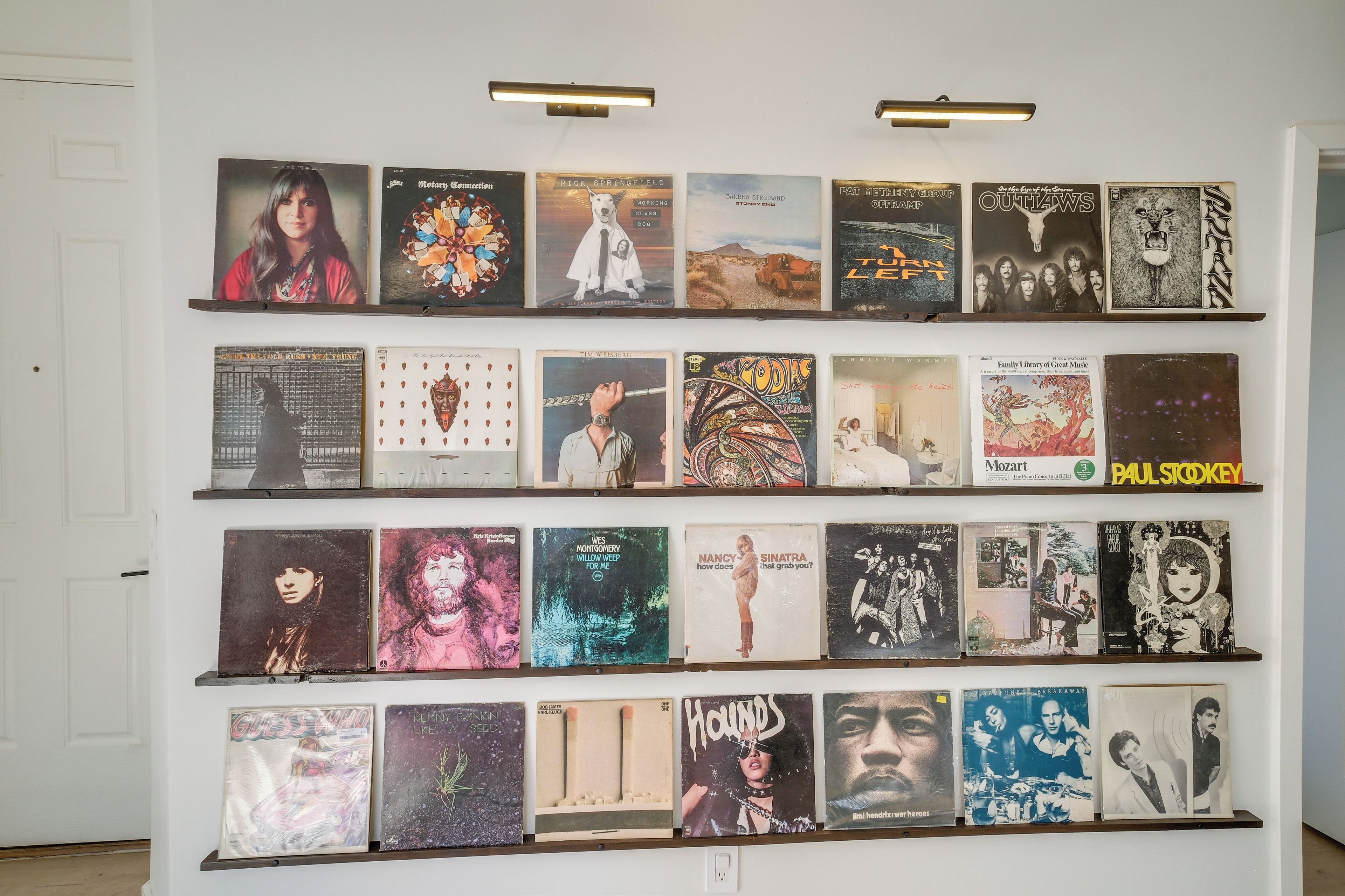 A wall with multiple rows of album covers displayed in a gallery setting.