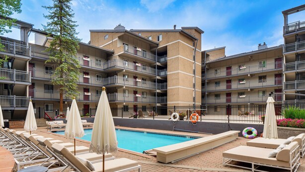 Uma área de piscina de hotel com espreguiçadeiras e guarda-sóis, cercada por edifícios com vários andares e varandas.