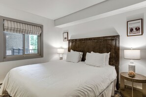 Une chambre d’hôtel avec un grand lit, deux lampes de chevet, une fenêtre donnant sur un beau paysage et un tableau encadré au mur.
