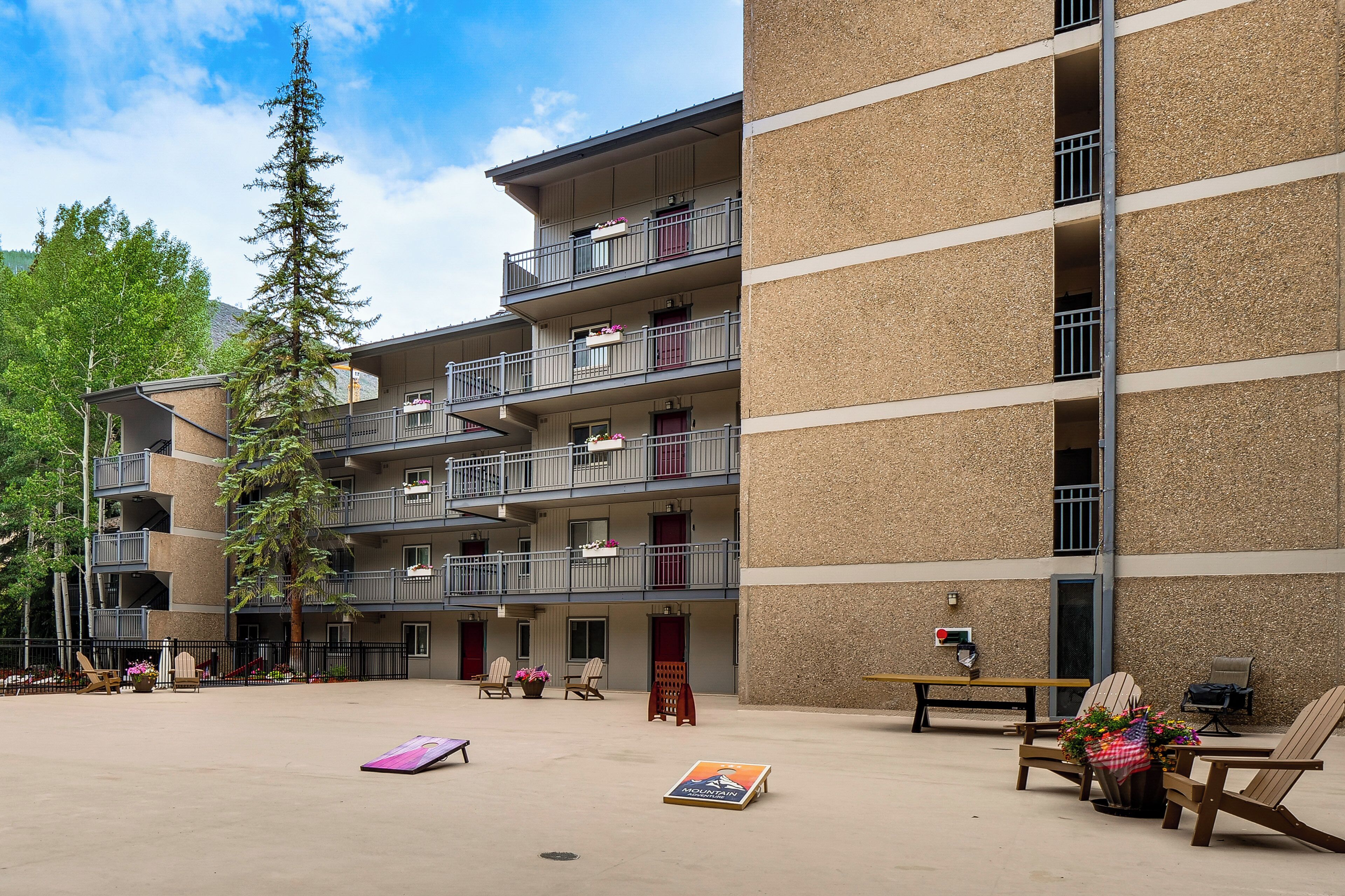 Un edificio de varios pisos con balcones, mesas al aire libre y un cielo despejado.
