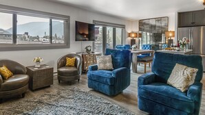 Uma sala de estar moderna com sofás de couro, uma poltrona azul, uma área de jantar e uma cozinha com uma grande janela.