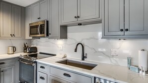 Uma cozinha moderna com armários cinza, eletrodomésticos de aço inoxidável e painel de fundo de mármore.