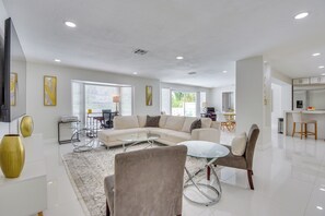 A modern living room with a sectional sofa, a glass coffee table, and a dining area in the background. - 6 Mi to Siesta Beach! Extended Getaway w/ Pool (Sarasota)