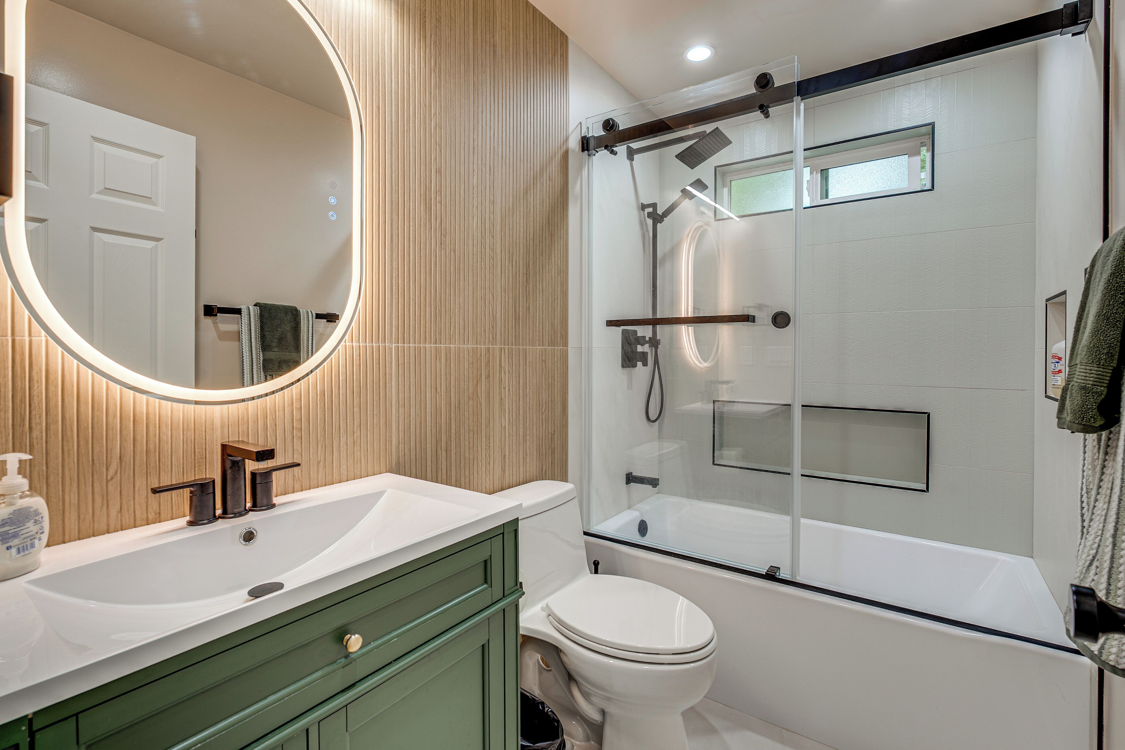 Un baño con ducha de vidrio, lavamanos blanco y tocador verde.
