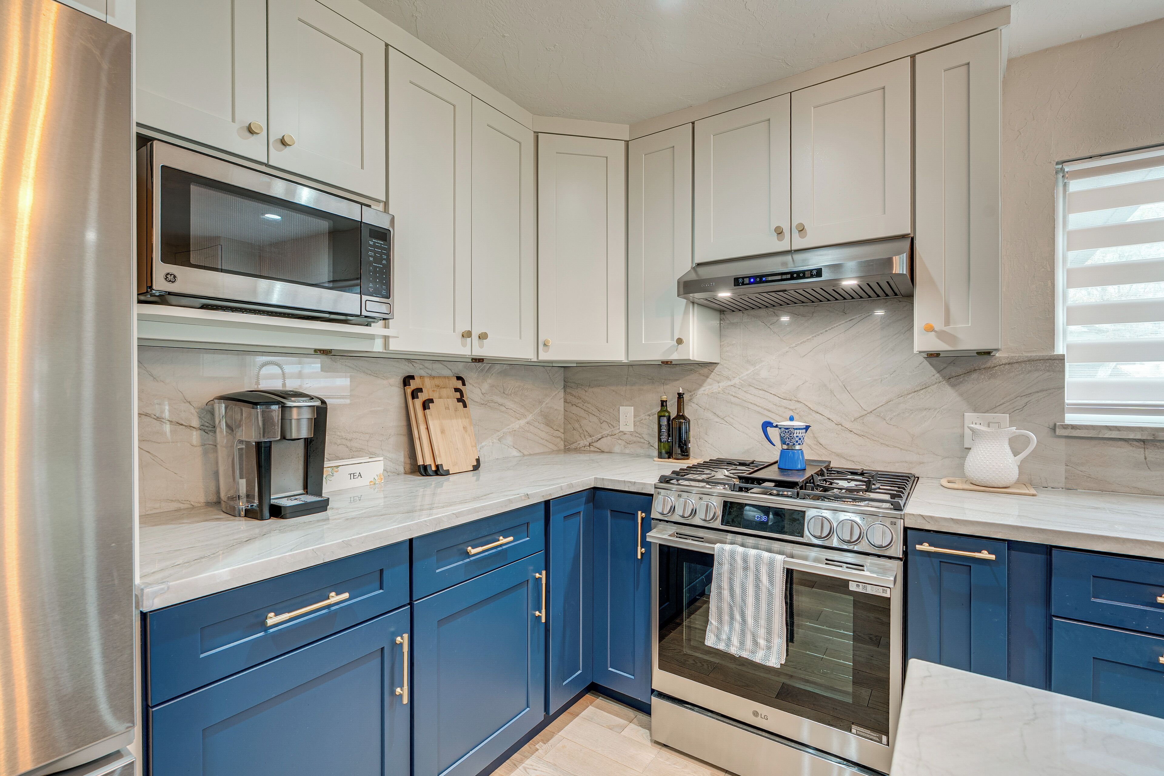 Una cocina moderna con electrodomésticos de acero inoxidable, armarios azules y encimera de mármol.