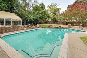 Ein Garten mit Swimmingpool, einer überdachten Terrasse und einem eingezäunten Bereich mit Bäumen und Sträuchern.