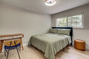 Ein Schlafzimmer mit Bett, Fenster, Heizkörper, Stuhl und kleinem Tisch.