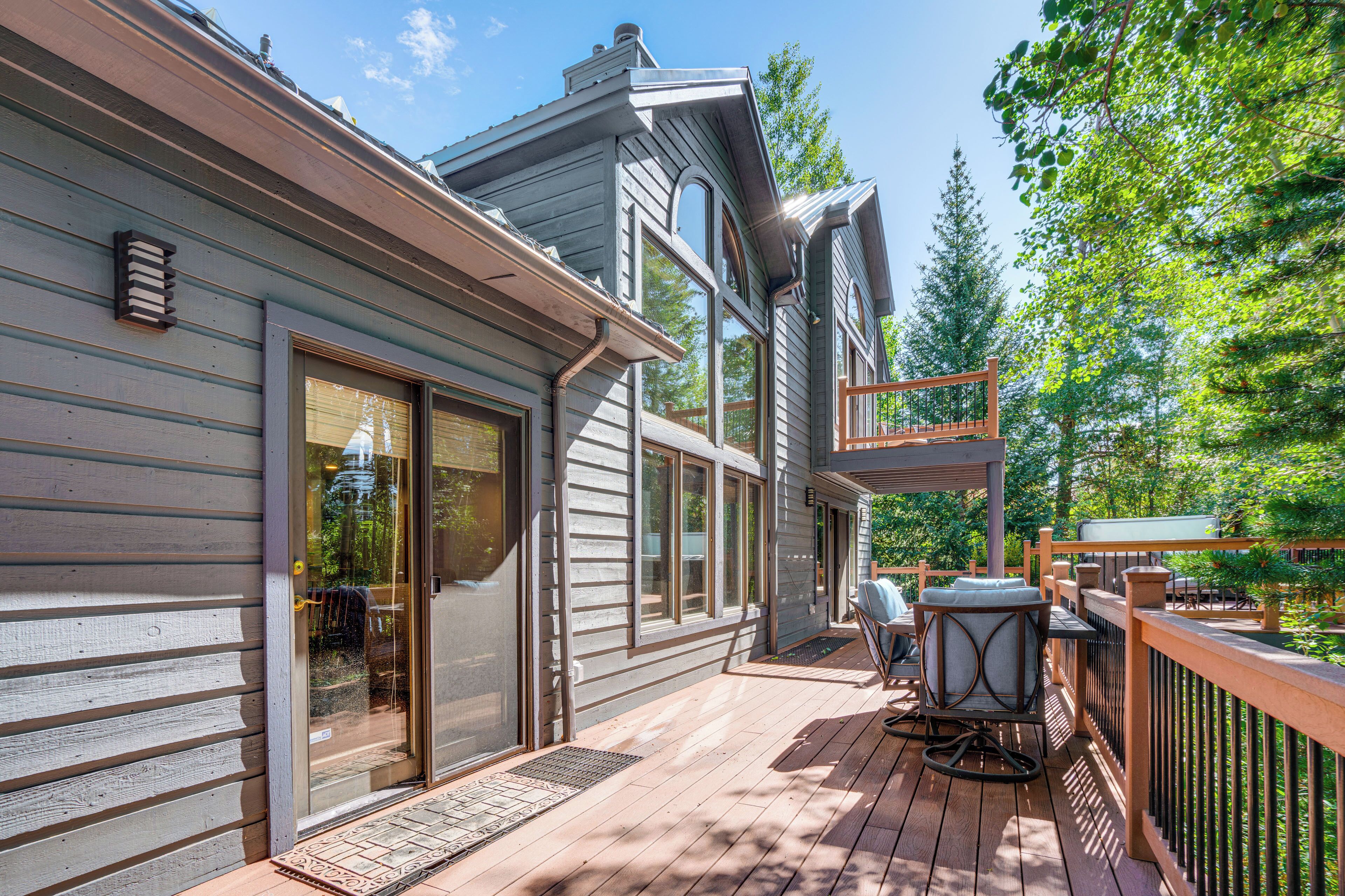 A wooden deck with outdoor furniture, a covered seating area, and a view of the surrounding trees.