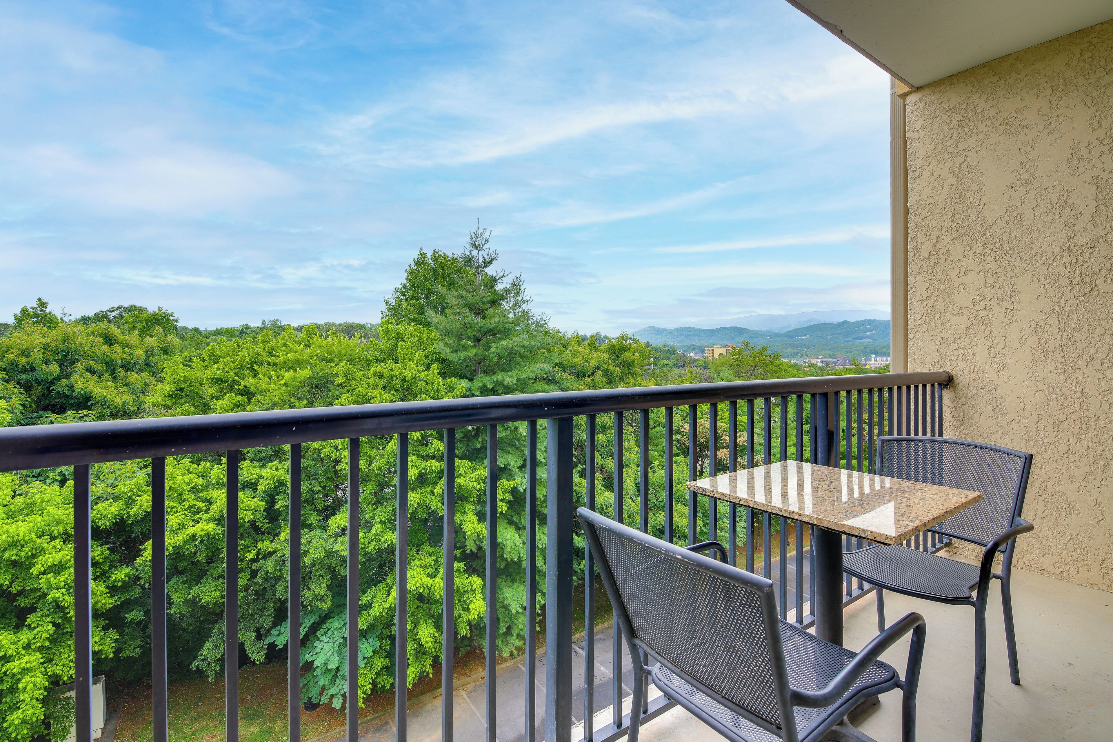 A balcony with a table and chairs, overlooking a lush green landscape and distant mountains.