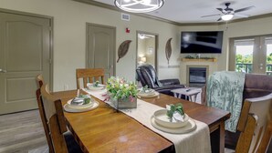 A dining area with a wooden table set for four, a television mounted on the wall, and a fireplace. - Mtn Views, Pool Access! Walkable Gem Near Parkway (Pigeon Forge)