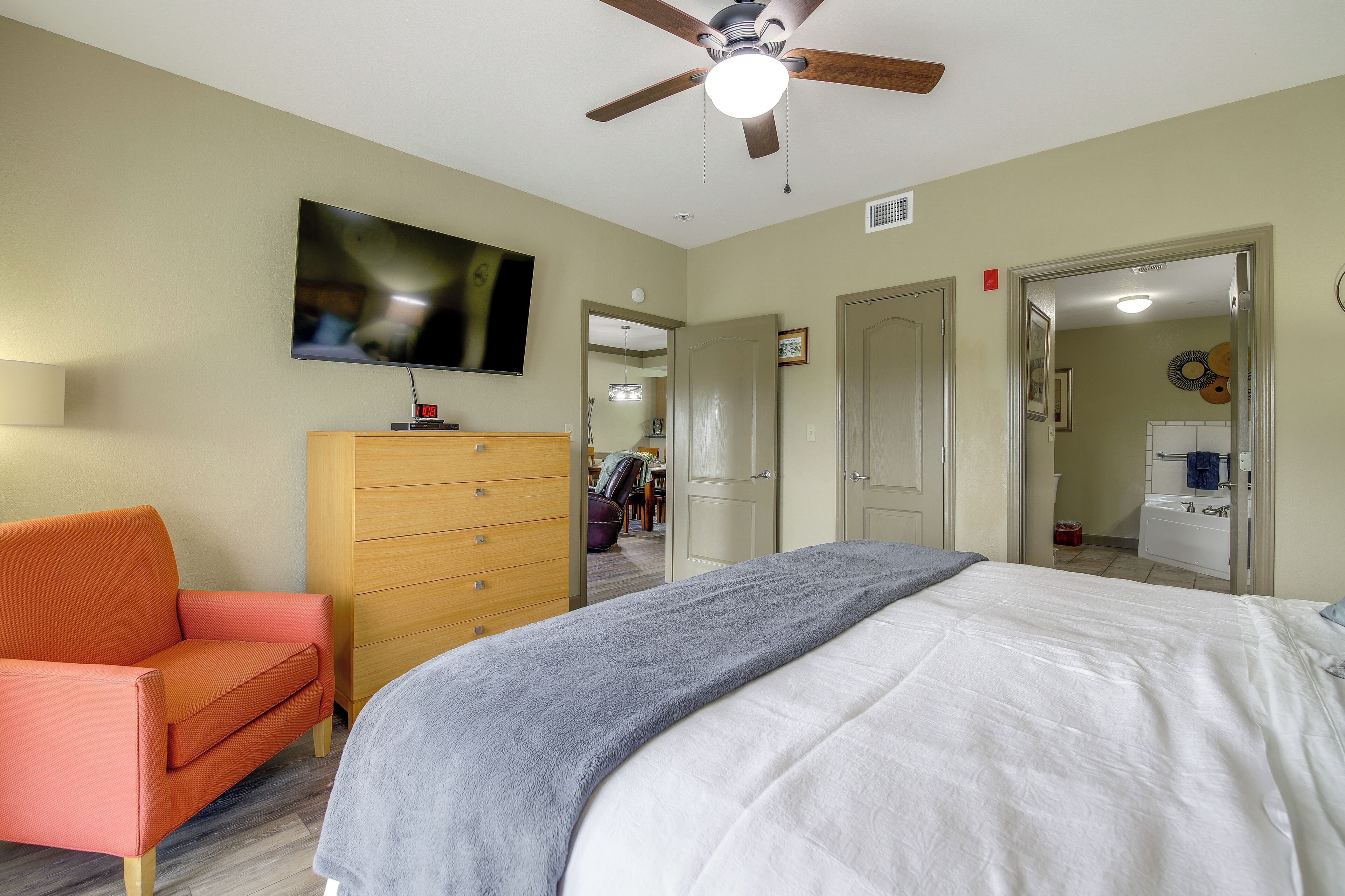 A hotel room with a bed, a television, a wooden dresser, a chair, and a bathroom visible through an open door.