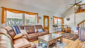 A spacious living room with a brown leather sectional sofa, a wooden coffee table, and a dining area with a chair and table.