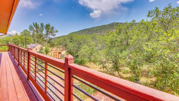 A wooden deck with a red railing overlooking a lush green landscape with trees and a hill in the distance. - Hiking Days, Fireside Nights! Colorado Springs Gem (Colorado Springs)