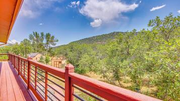 A wooden deck with a red railing overlooking a lush green landscape with trees and a hill in the distance.