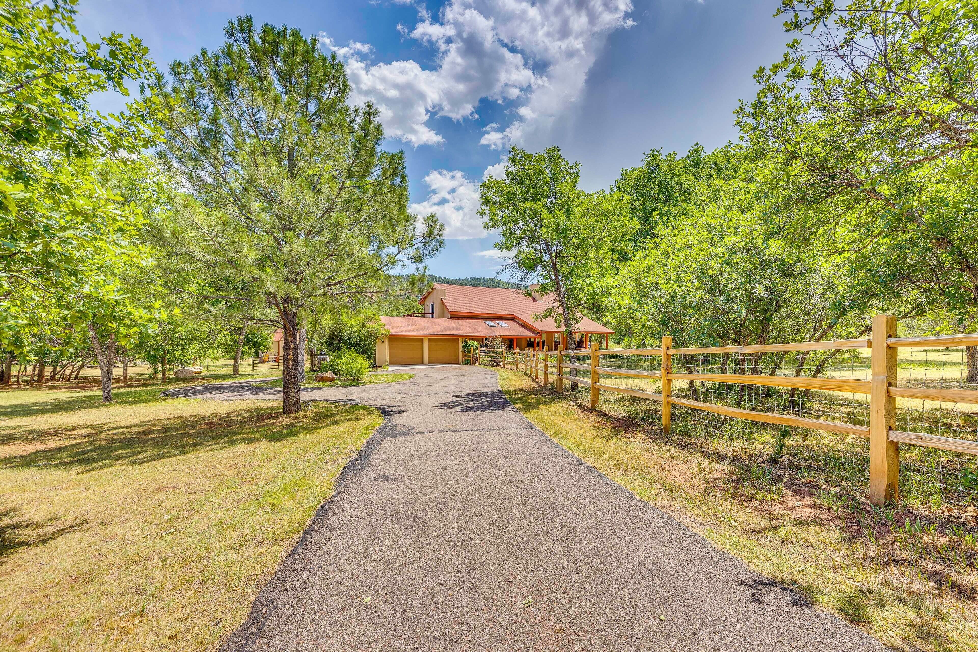 A paved pathway leading to a building with a red roof, surrounded by trees and a wooden fence.