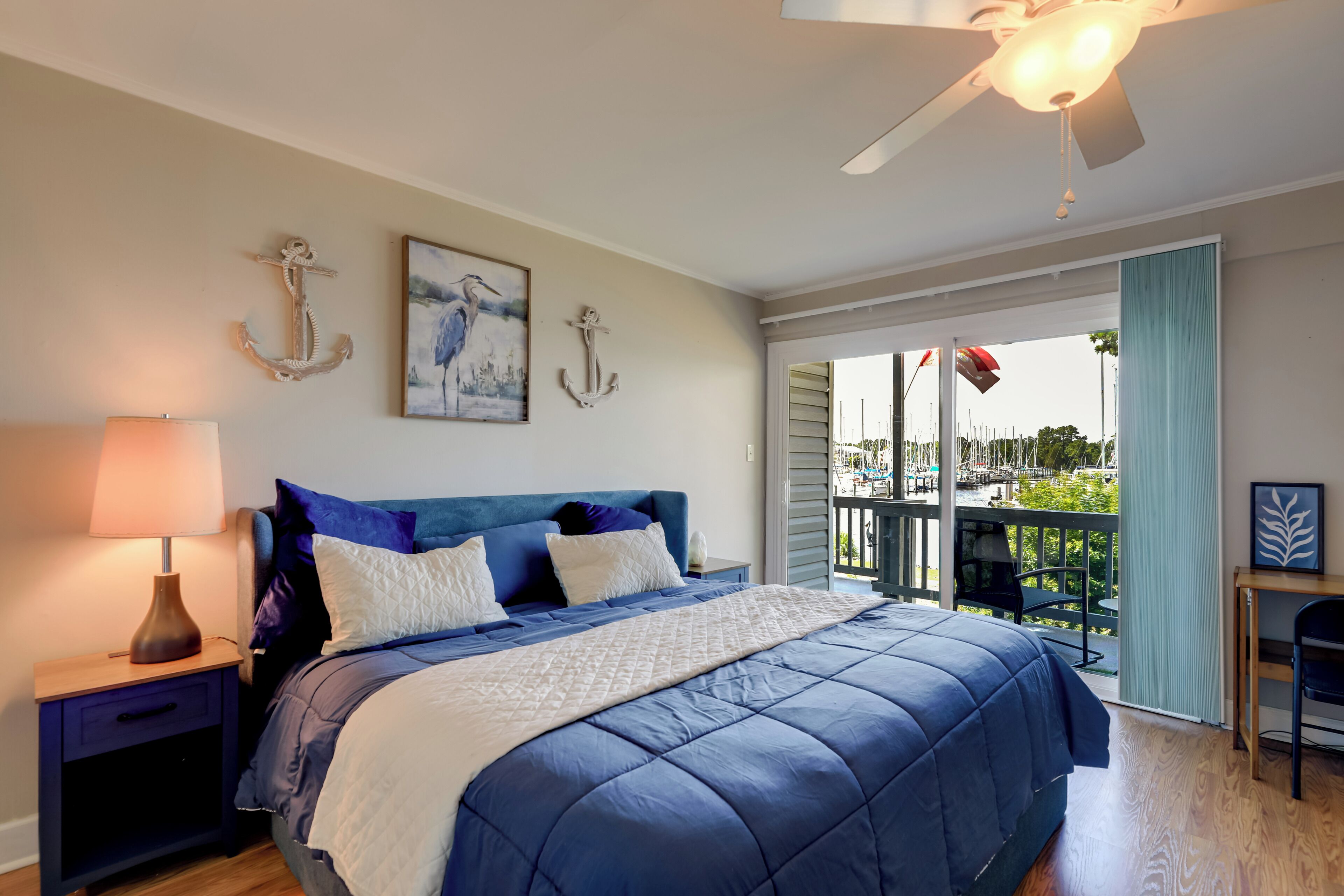 A bedroom with a bed, a nightstand, a lamp, and a view of the outside.