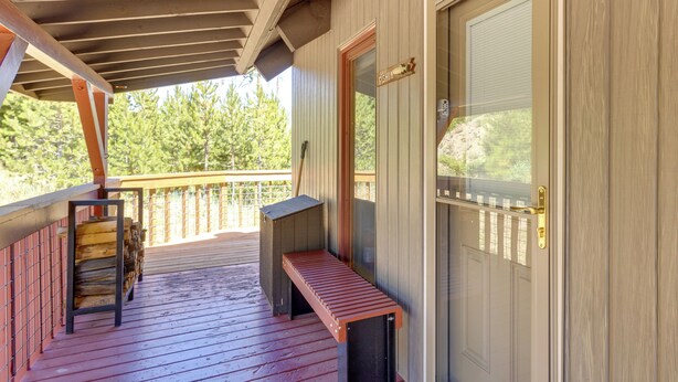 Un terrazzo in legno con una panchina, una porta con una cassetta delle lettere e vista sugli alberi.