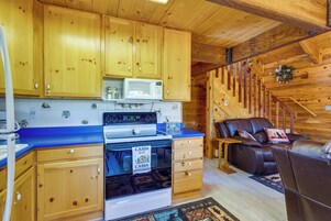 A cabin interior with wooden cabinets, a microwave, a stove, a sofa, and a staircase.