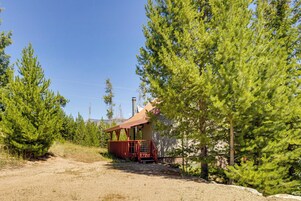 A rustic cabin with a wooden deck, surrounded by dense evergreen trees.
