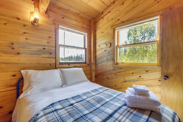 Un dormitorio de cabaña de madera con una cama, una ventana y una mesita de noche con toallas.