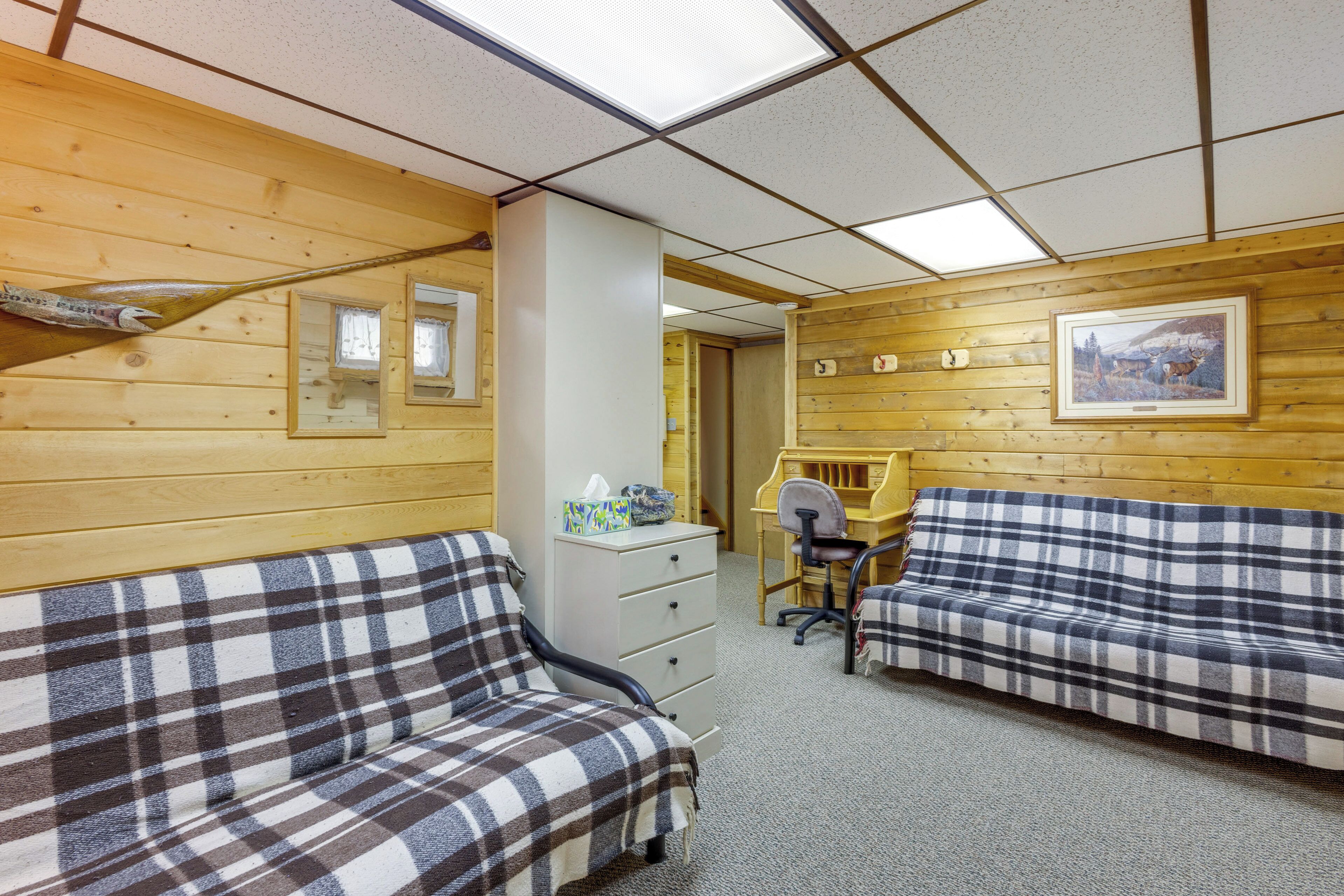 A room with wooden walls, two plaid sofas, a desk, and a chair.