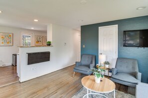 A modern living room with a flat-screen TV mounted on the wall, two grey armchairs, a coffee table with a plant, and a wooden floor. - 1 Mi to Olde Town Arvada! Updated Home w/ Patio (Arvada)