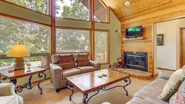 A cozy living room with a fireplace, large windows, and a television. - Golf Getaway w/ Fairway Views Near Table Rock Lake (Eureka Springs)
