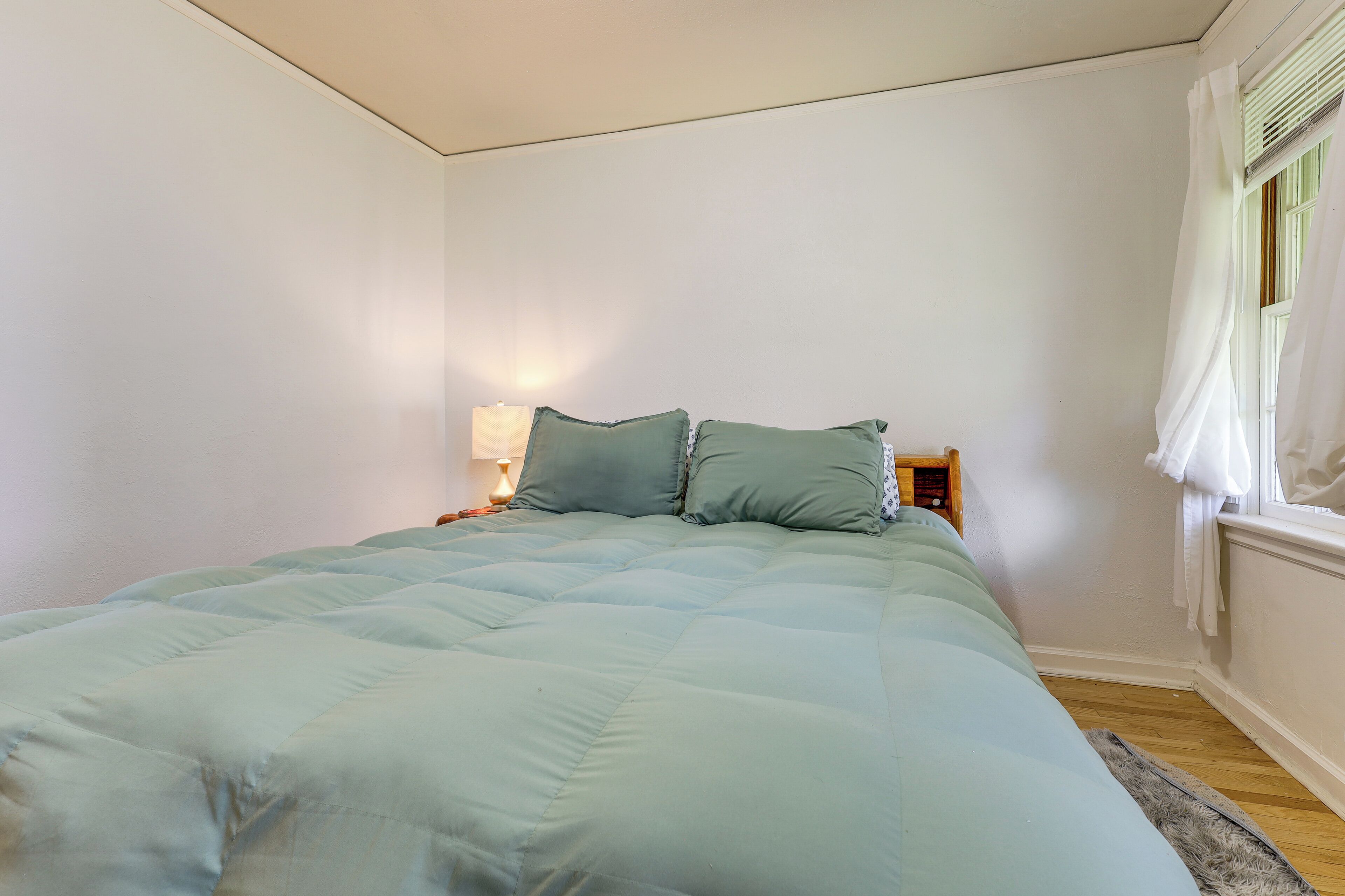 A bedroom with a bed, a nightstand, a lamp, and a window with curtains.