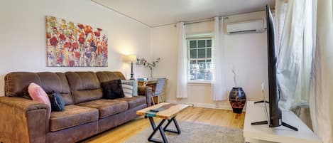 A living room with a brown leather sofa, a wooden coffee table, a flat-screen TV, and a large floral painting on the wall.