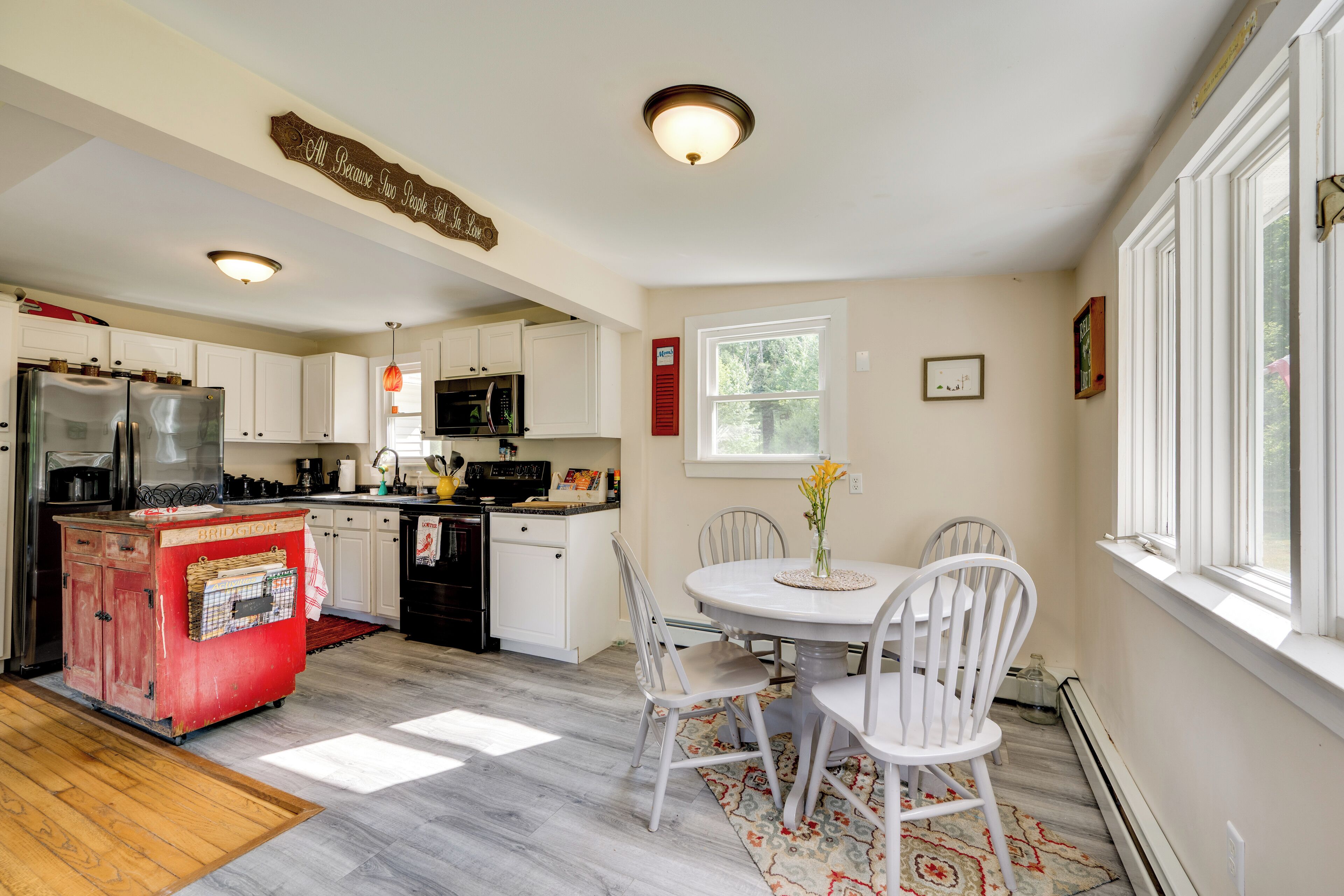 Una cocina con gabinetes blancos, un refrigerador rojo de estilo vintage y una zona de comedor con sillas y una mesa blancos.